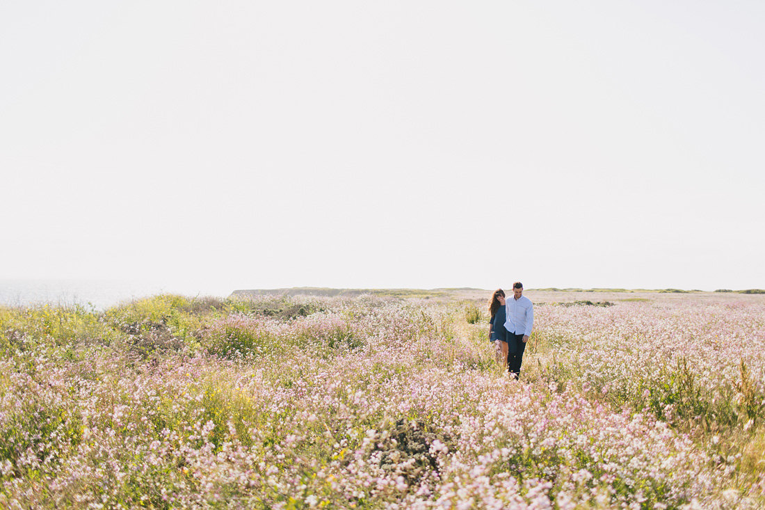 Engaged couple walking in field of wildflowers